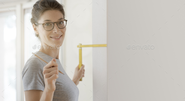 Smiling woman doing a home makeover and measuring with a ruler