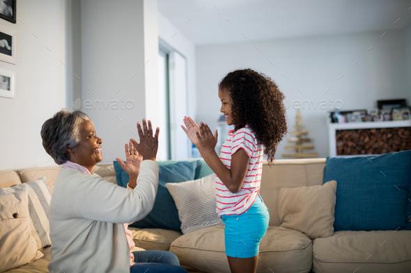 Granddaughter and grandmother playing clapping games on sofa in living room