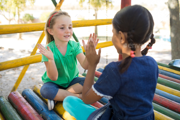 Girls playing clapping game while sitting on jungle gym