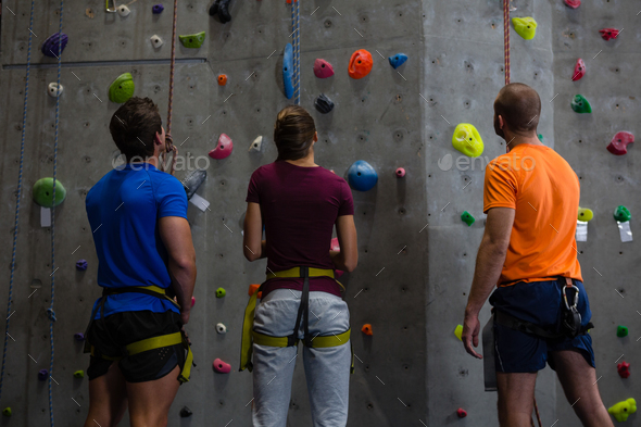 Rear view of trainer with athletes standing by climbing wall