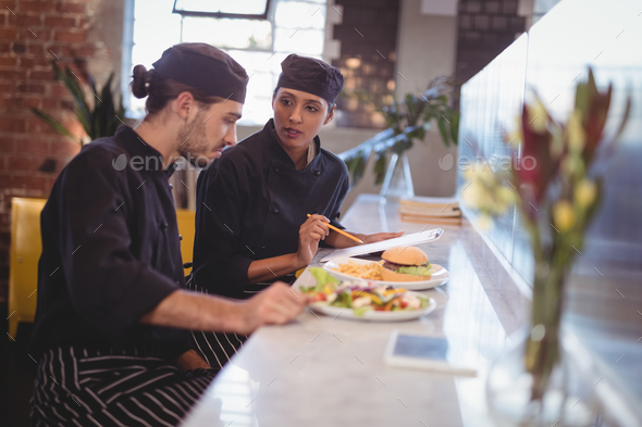 Young wait staff discussing over clipboard and food while sitting at counter