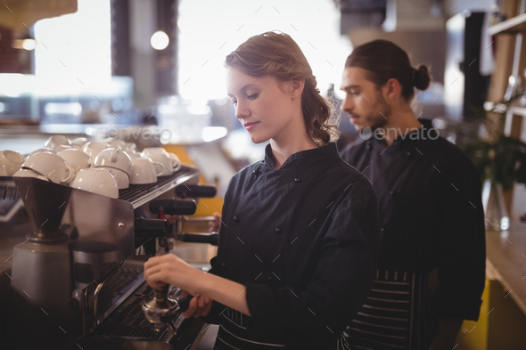 Young wait staff using espresso maker at coffee shop