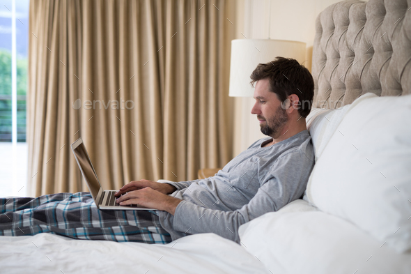 Man using laptop bed Stock Photo Wavebreakmedia | PhotoDune