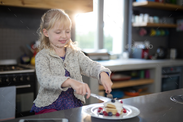 Little girl cutting a fruit pancake with a fork and knife Little girl cutting a fruit pancake with a fork and knife