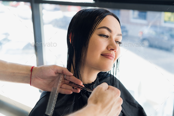 Male hairdresser making a haircut for a beautiful brunette girl in professional hairdressing salon.