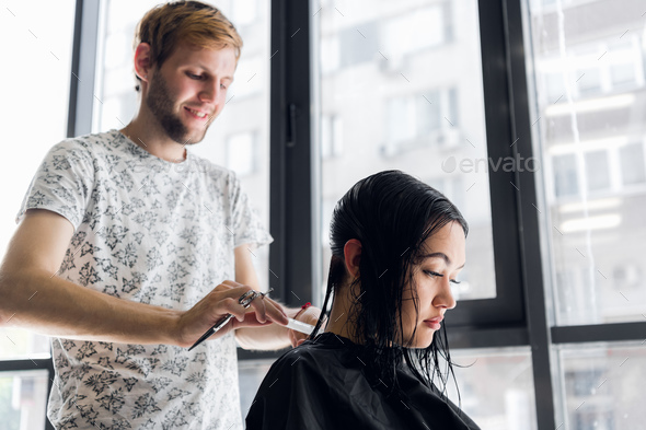 Young beautiful woman having her hair cut at the hairdresser's. Young male hairdresser smiling - Stock Photo - Images