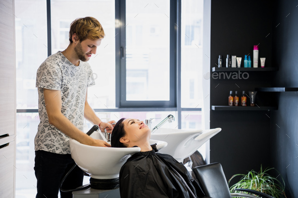 Man hairdresser washing head client. A man hair master watering a girl's hair with a shower in a
