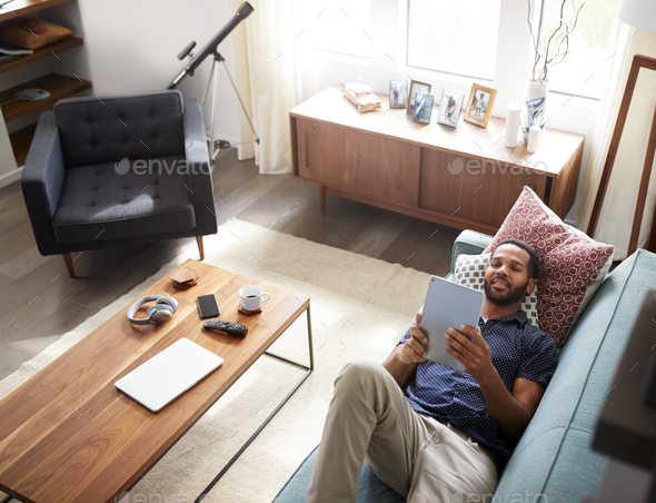 Overhead View Of Man Lying On Sofa At Home Watching Movie On Digital Tablet