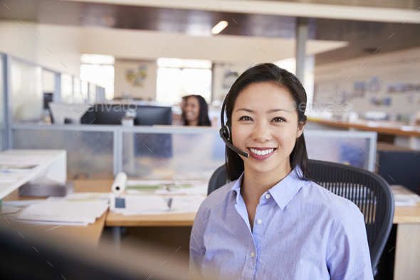 Young Asian woman working in a call centre smiling to camera - Stock Photo - Images