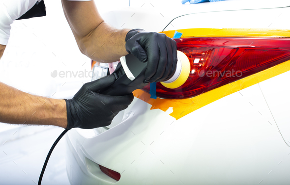 The man is polishing red back lights of a modern white car with polish machine