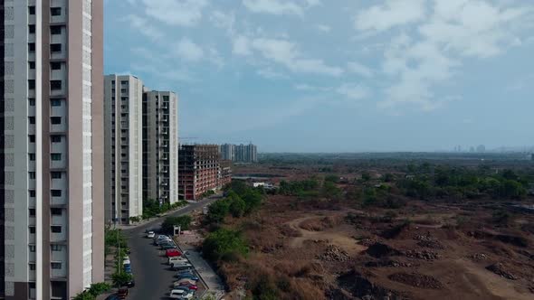 Drone moving towards Buildings in India with dry land and greenery on the other side alt