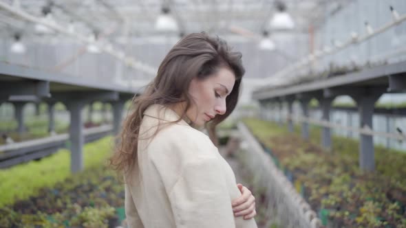 Young Brunette Caucasian Woman Turning To Camera As Standing in Greenhouse. Enigmatic Lady with alt
