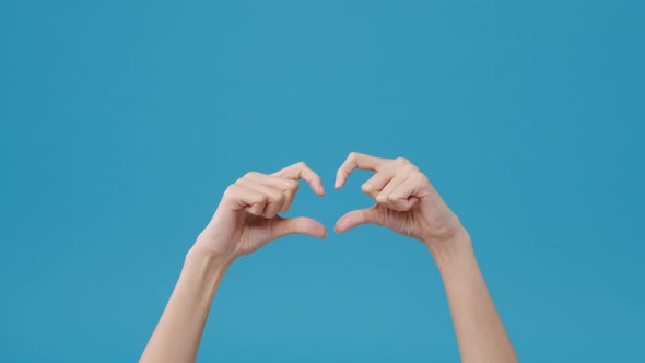 Young woman hand shows making shape of heart sending love to her lover over blue background.
