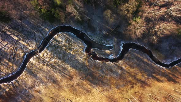 View From the Copter Down on a Narrow River in the Forest on the Edges of Which Lies the First Snow