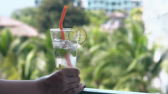 Girl Holds Glass with Frozen Drink on Hotel Room Balcony alt