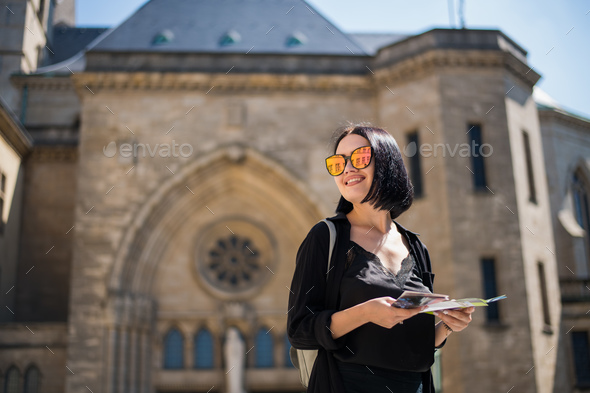 Brunette young woman tourist holding a city map and searching right direction standing outdoors in - Stock Photo - Images