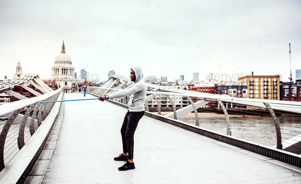 Young active black sportsman exercising with elastic rubber bands in London.