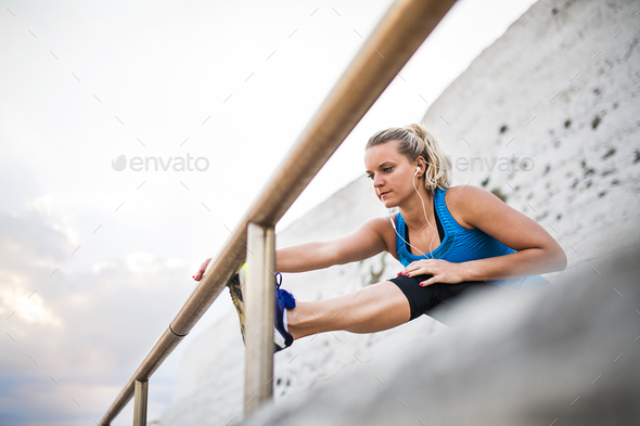 Young sporty woman runner with earphones stretching on the beach outside. - Stock Photo - Images