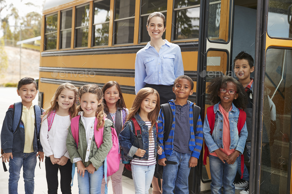 Elementary school teacher and pupils standing by school bus