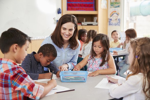 Teacher sitting at table with young school kids in classroom Stock ...