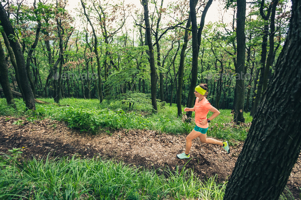 Young woman trail running in mountains on forest trail, sunny da - Stock Photo - Images