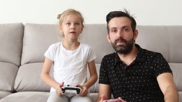 Father and Young Child are Playing Video Game on Couch at Home Pressing Buttons on Joystick