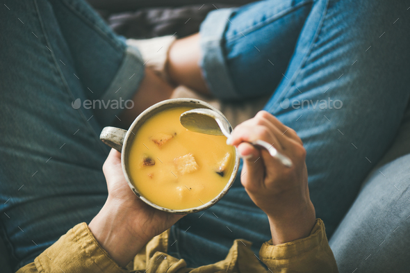 Female keeping mug of warming pumpkin yellow cream soup - Stock Photo - Images