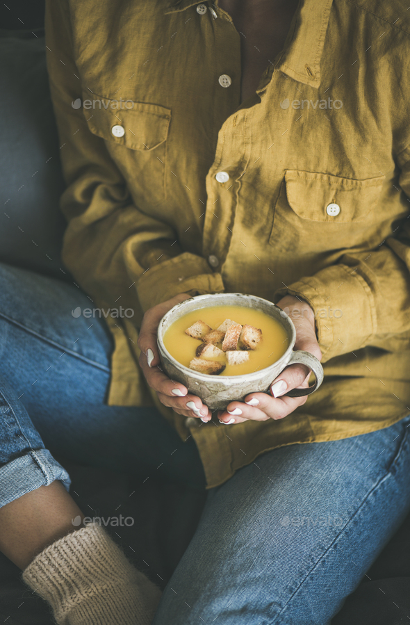 Woman sitting and holding warming pumpkin soup in mug - Stock Photo - Images