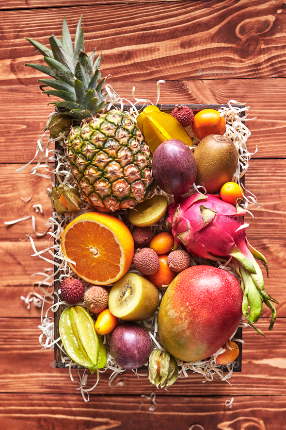 The box with exotic tropical fruits - fresh ripe pineapple, mango, dragon fruit, orange, carambola