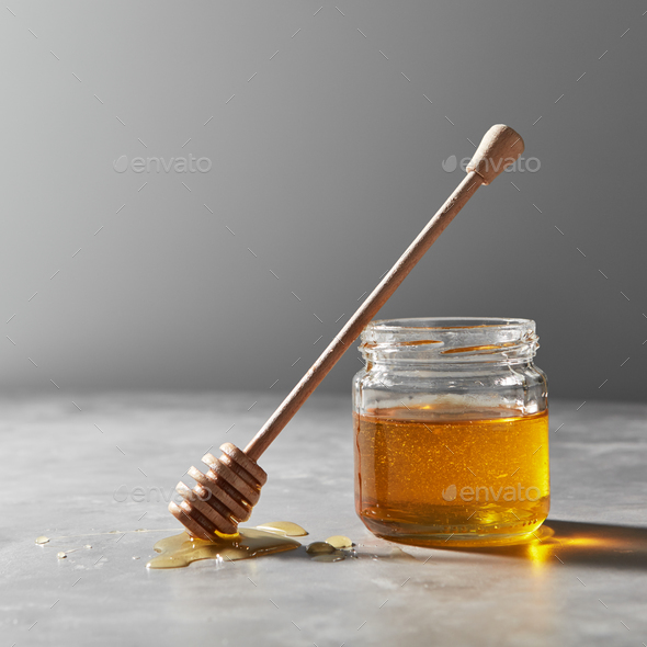 A puddle of fresh flower honey on the table with glass pot with natural dessert on a gray concrete