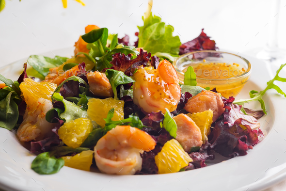 Healthy salad with prawns, lettuce, oranges and mango served on a plate with orange mustard sauce - Stock Photo - Images