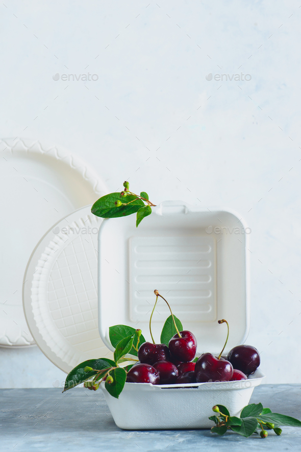 Eco-friendly food packaging with cherries. White containers, plates and other catering disposables