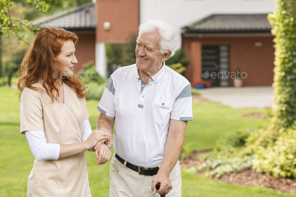 Smiling grey-haired senior man with a walking stick talking talk - Stock Photo - Images