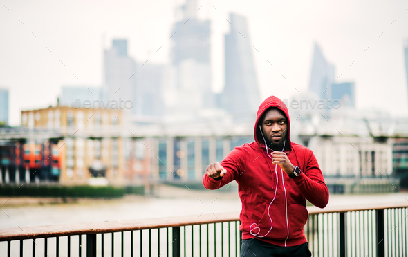 A black man runner with earphones and hood on his head in a city. Copy space.
