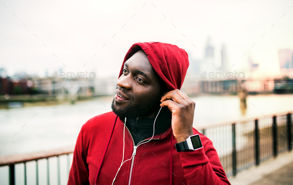 A close-up of black man runner with earphones and hood on his head in a city. Copy space.