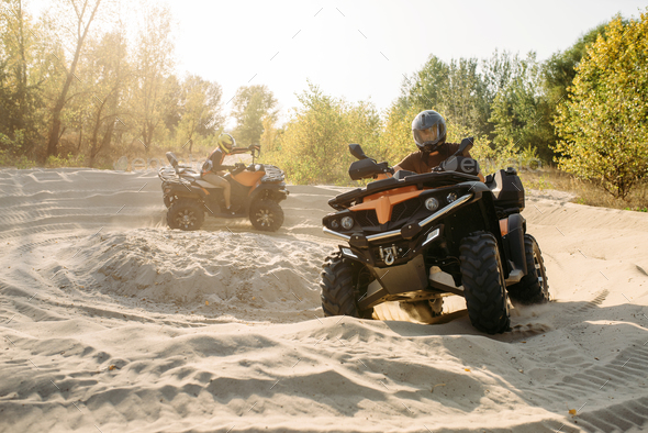 Two atv riders in helmets ride in a circle on sand - Stock Photo - Images