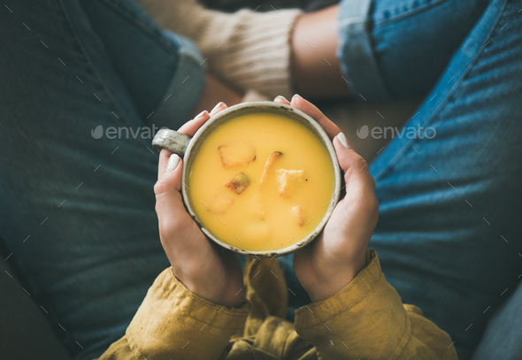 Female keeping mug of pumpkin yellow cream soup in hands - Stock Photo - Images