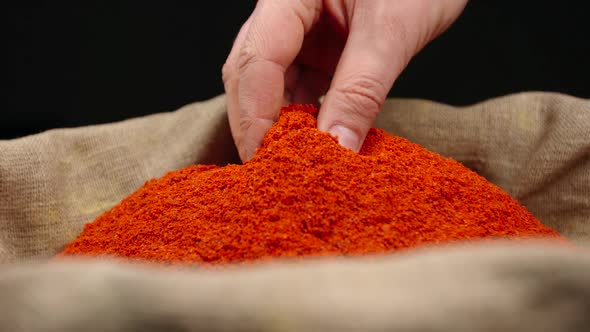 Human hand takes a pinch of a red pepper powder from a top of pile in a sac
