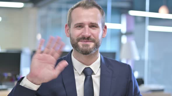 Portrait of Young Businessman Waving at Camera in Office alt