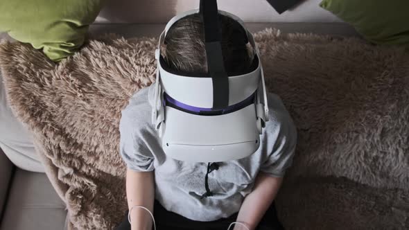 Young Woman in Virtual Reality Helmet Sitting on Sofa and Move Hands at Home alt