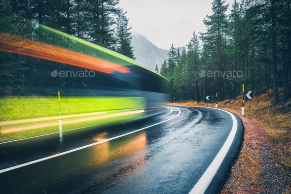Blurred green bus on the road in autumn forest in rain - Stock Photo - Images