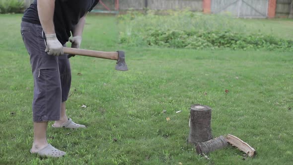 Men's Hands Chop Firewood with an Ax on a Special Stump on the Background of Beautiful Green Grass