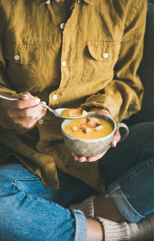 Woman sitting and eating pumpkin soup from mug - Stock Photo - Images