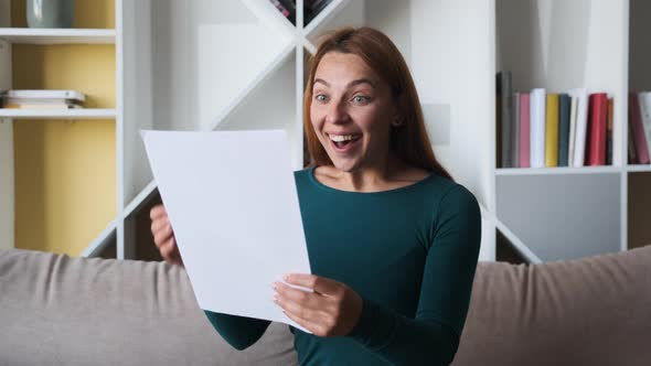 Happy Young American Woman Reading Paper Letter, Amazed By Good News, Sitting on Sofa at Home alt