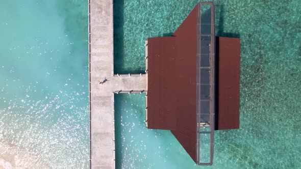 Woman standing on pier boat house of Gili Meno during beautiful summer day.Ascending aerial top down alt