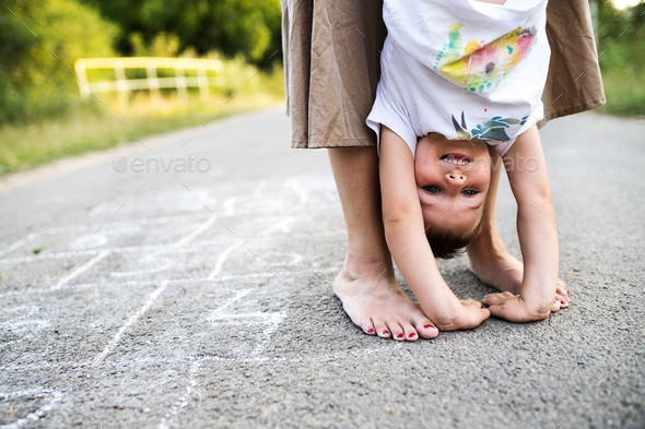 Unrecognizable mother holding a small son upside down on a road in park in summer.