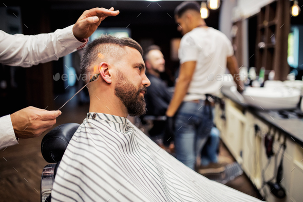 Hipster man client visiting haidresser and hairstylist in barber shop ear hair removal