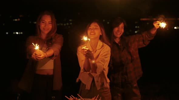 group of young Asian friends are having fun playing fireworks during a summer camping vacation.
