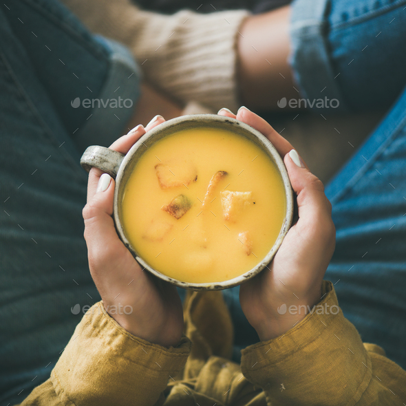 Female keeping mug of pumpkin yellow cream soup, square crop - Stock Photo - Images