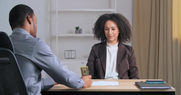Afro American Businessman Sitting at Table Back To Camera Giving Professional Woman Money Banknotes alt